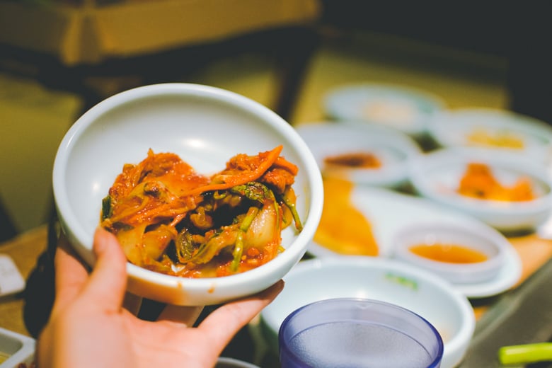 A bowl of kimchi held over a table of side dishes