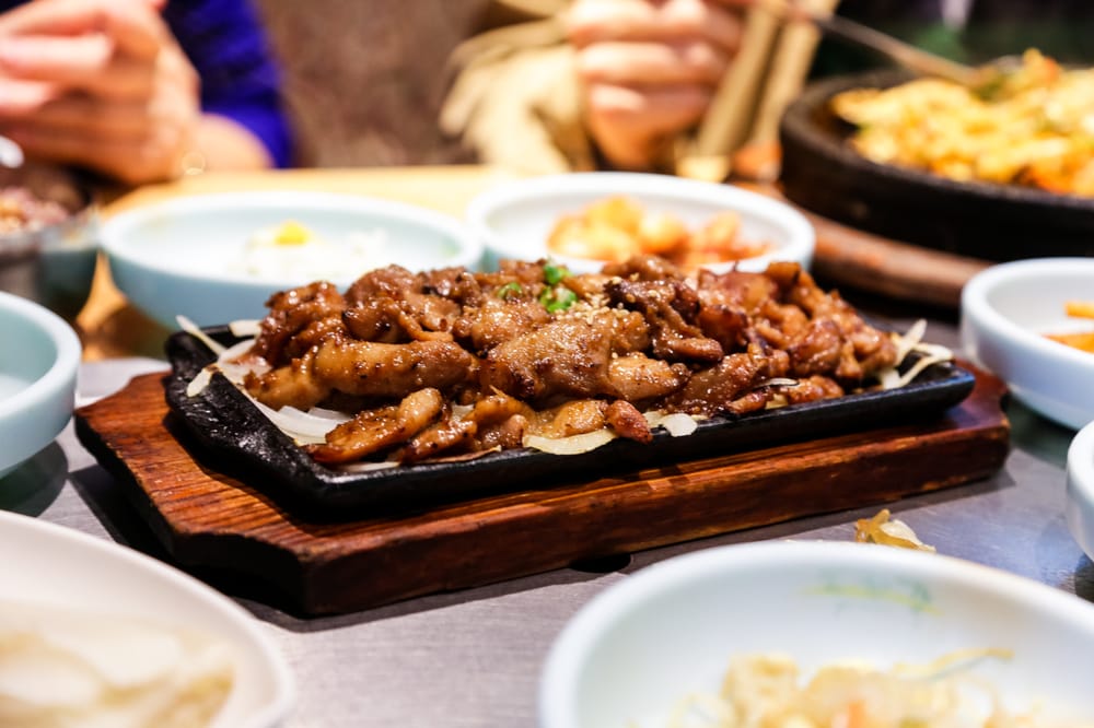 Marinated beef sizzling on a hot plate, surrounded by side dishes